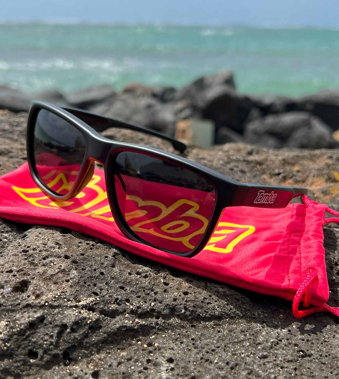 Tamba Sunglasses (Matte Black) sitting on a rock by a beach.  SKU#210000029012